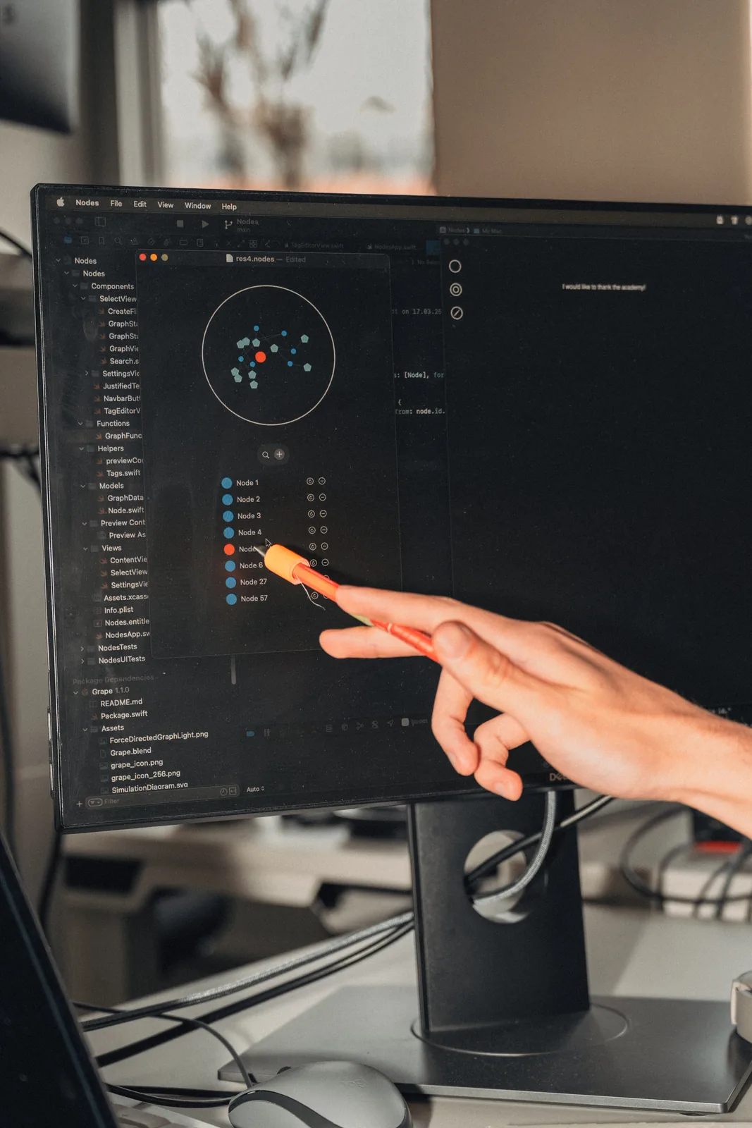 A hand pointing with an orange pencil at the first Nodes graph on a monitor: a ring of dots, and a list beside it reading Node 1 to Node 57.